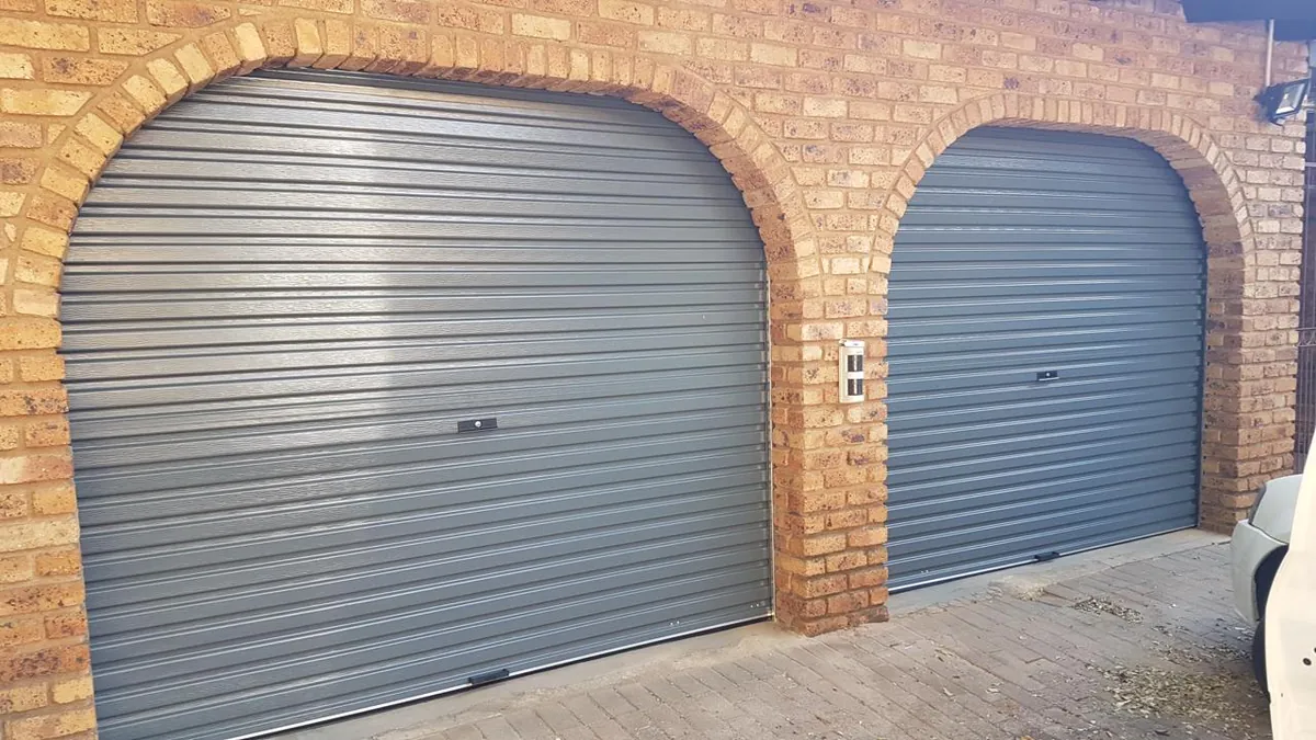 Two charcoal roll-up garage doors beneath brick arches, photographed on our own project